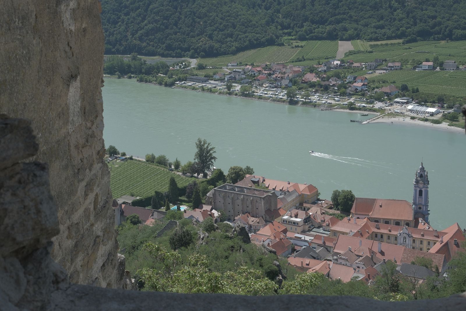 View through an old stone wall over Durnstein’s blue church tower and the Danube in the Wachau, on many cheap river cruises in Europe